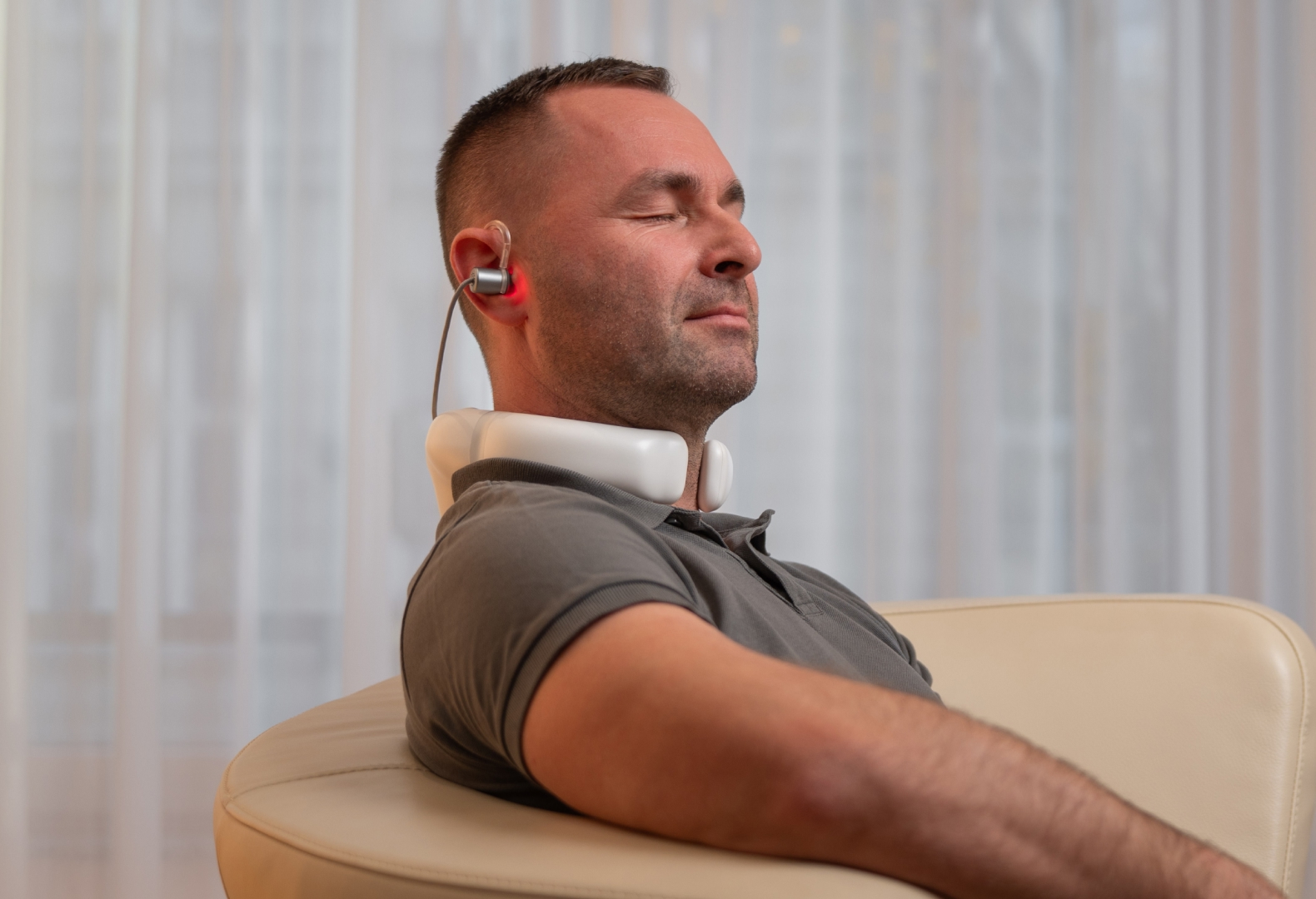 LumoHome Lasertherapie Mann sitzt entspannt im Wohnzimmer und nutzt den LumoHome Laser zur sanften Anwendung am Innenohr.“