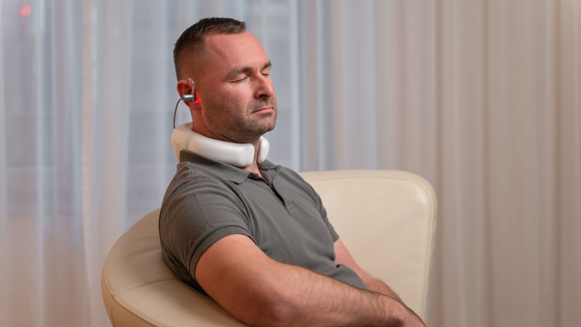 LumoHome Lasertherapie Mann sitzt entspannt im Wohnzimmer und nutzt den LumoHome Laser zur sanften Anwendung am Innenohr.“