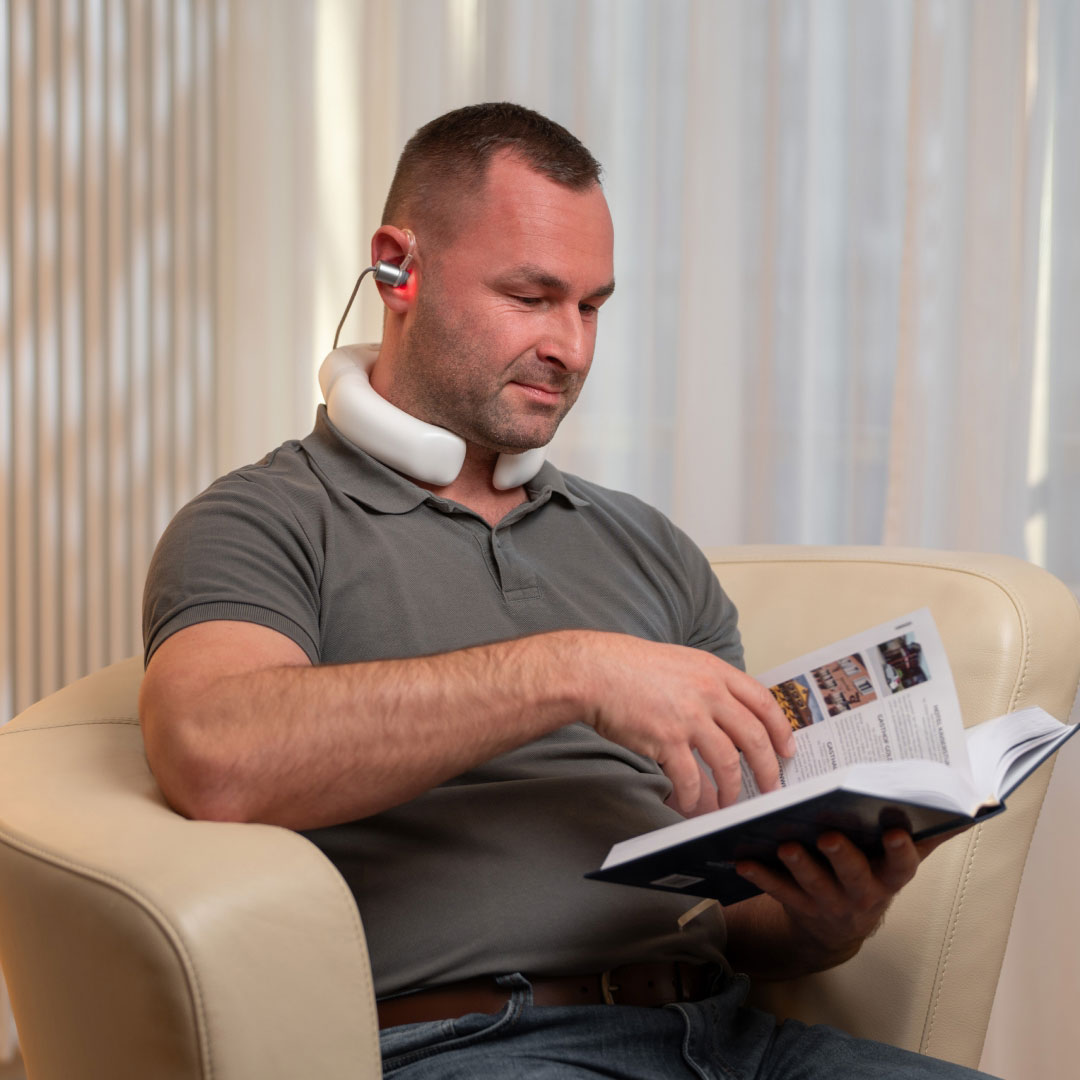 LumoHome Lasertherapie Mann sitzt entspannt im Wohnzimmer und nutzt den LumoHome Laser zur sanften Anwendung am Innenohr.“