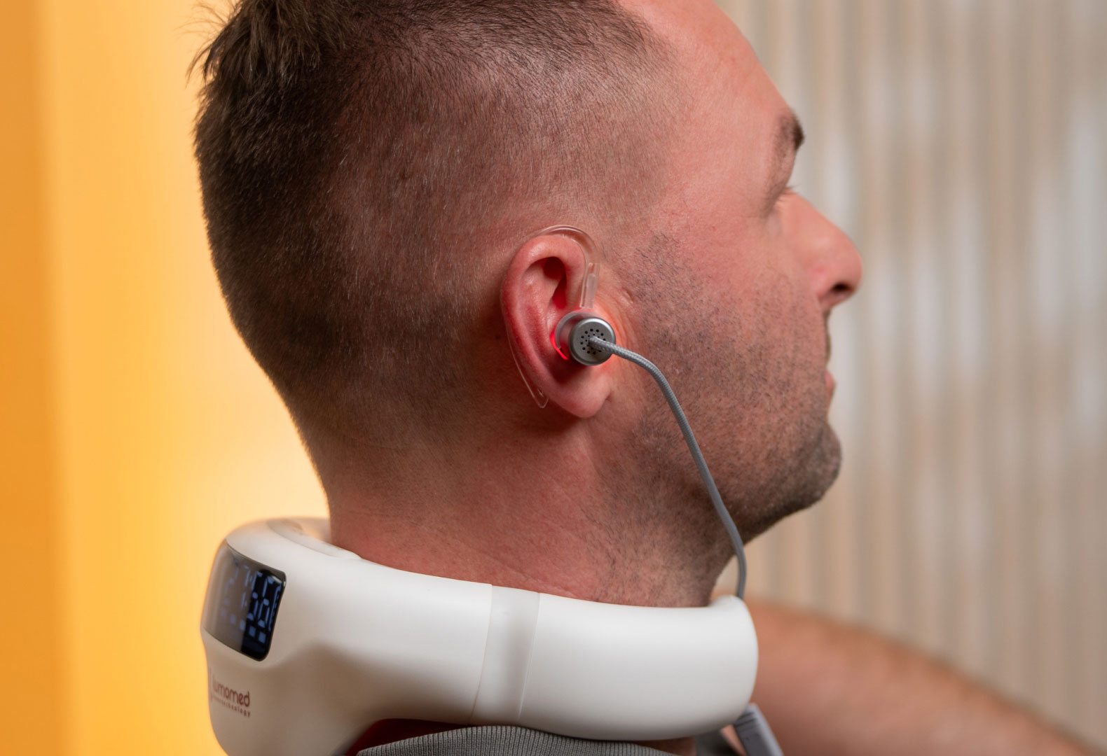 LumoHome Lasertherapie Mann sitzt entspannt im Wohnzimmer und nutzt den LumoHome Laser zur sanften Anwendung am Innenohr.“