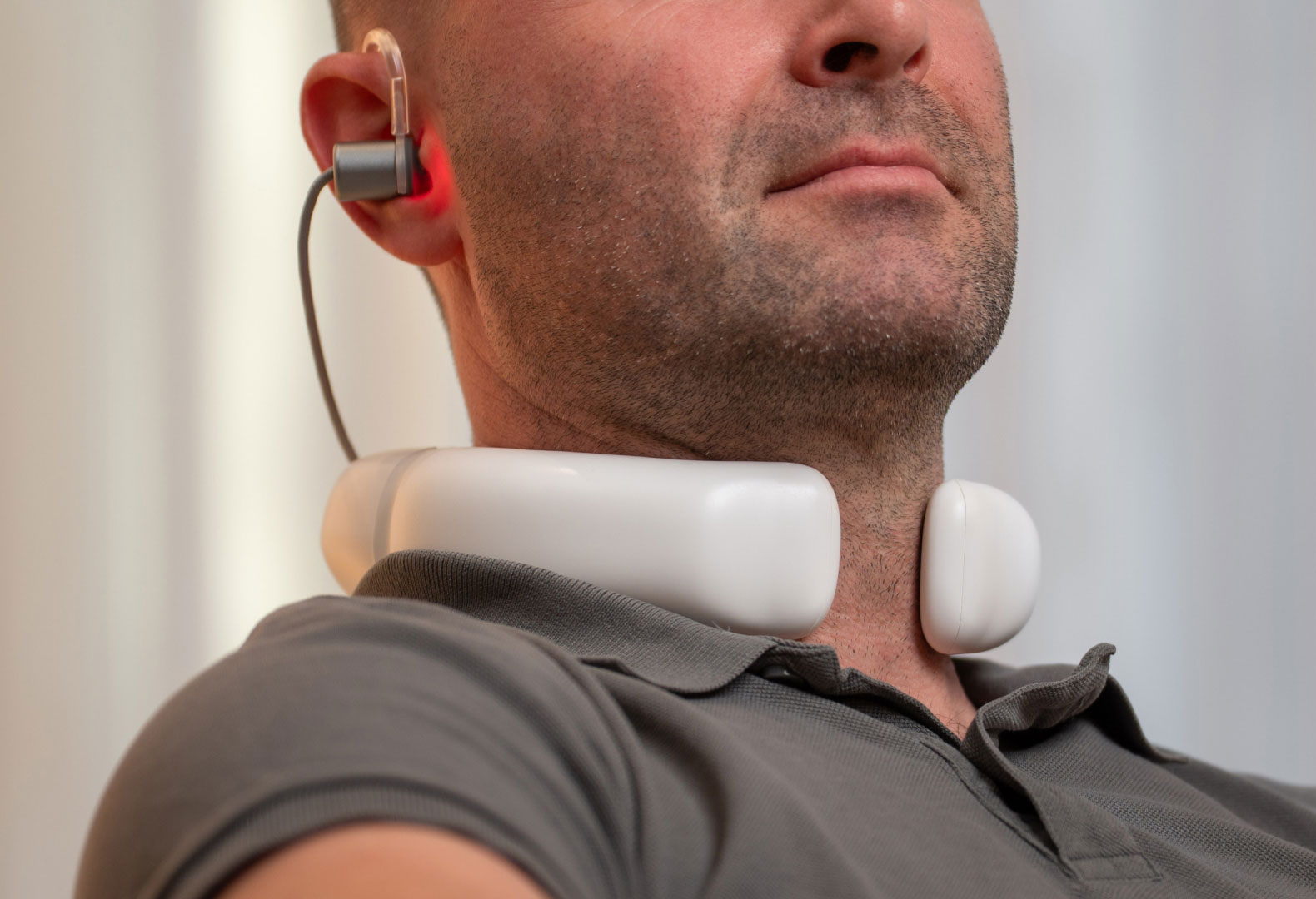 LumoHome Lasertherapie Mann sitzt entspannt im Wohnzimmer und nutzt den LumoHome Laser zur sanften Anwendung am Innenohr.“