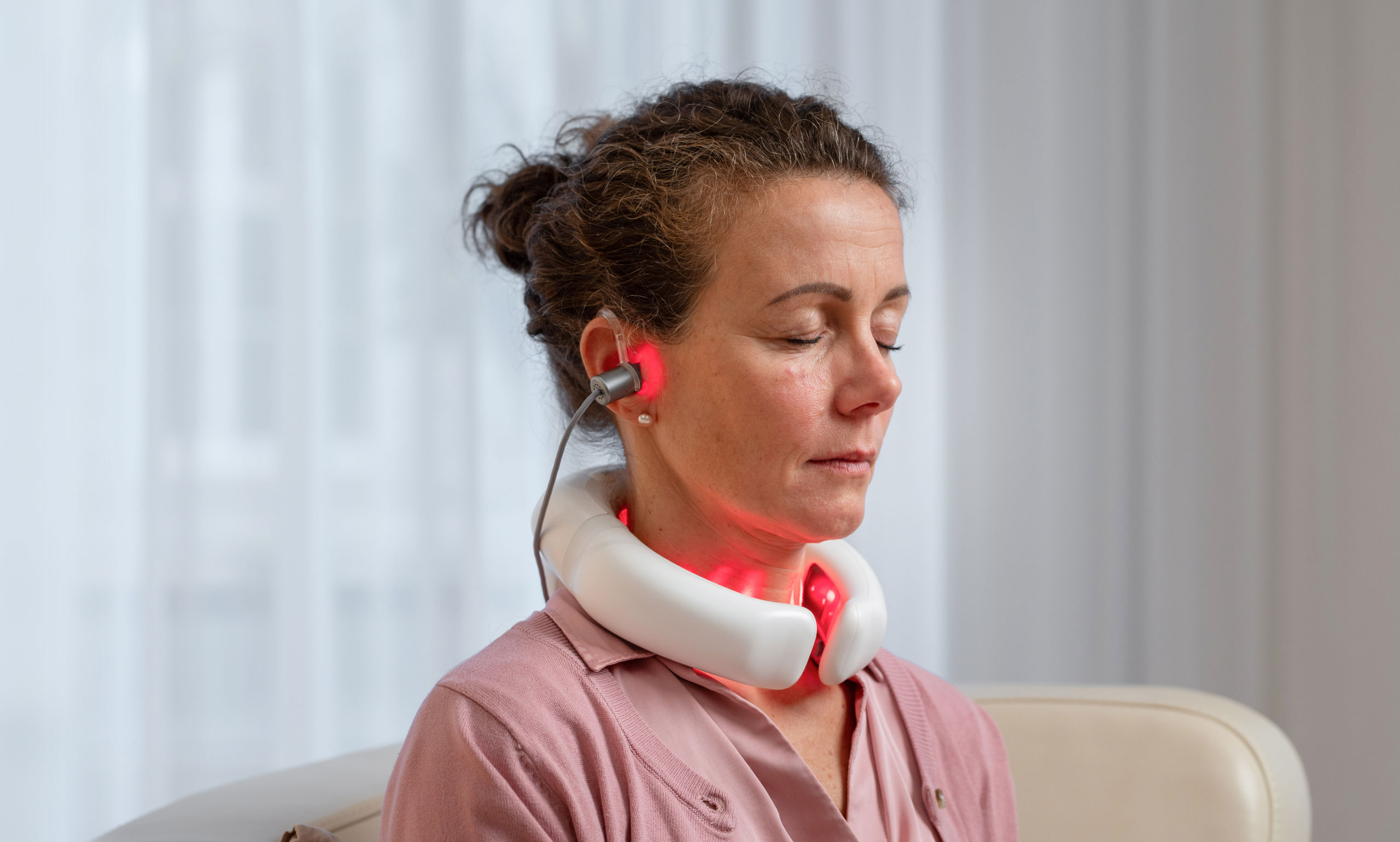 Frau sitzt entspannt im Wohnzimmer und nutzt den LumoHome Laser zur sanften Anwendung am Innenohr.“