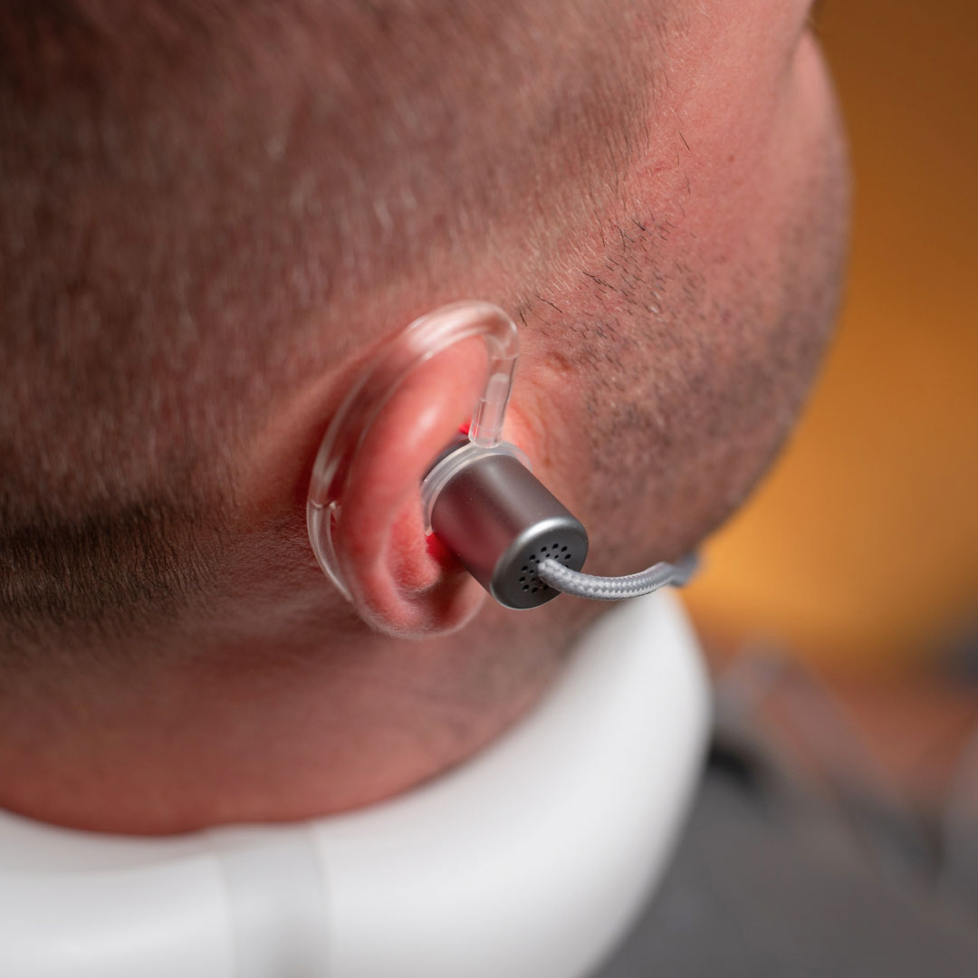 Mann sitzt entspannt im Wohnzimmer und nutzt den LumoHome Laser zur sanften Anwendung am Innenohr.“