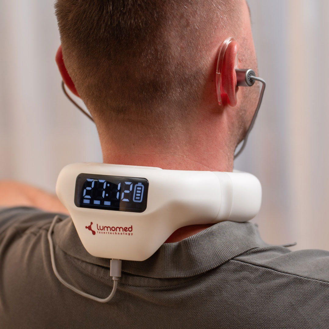 Mann sitzt entspannt im Wohnzimmer und nutzt den LumoHome Laser zur sanften Anwendung am Innenohr.“